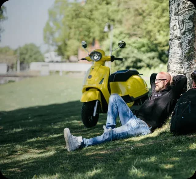 Man relaxing under a tree with a yellow scooter nearby