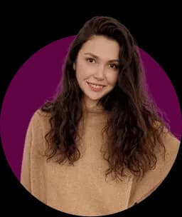 Smiling young woman with long curly hair wearing a light brown sweater in front of a pink circular background.