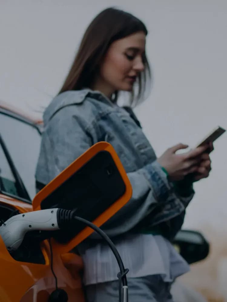 Woman using phone beside electric vehicle charger