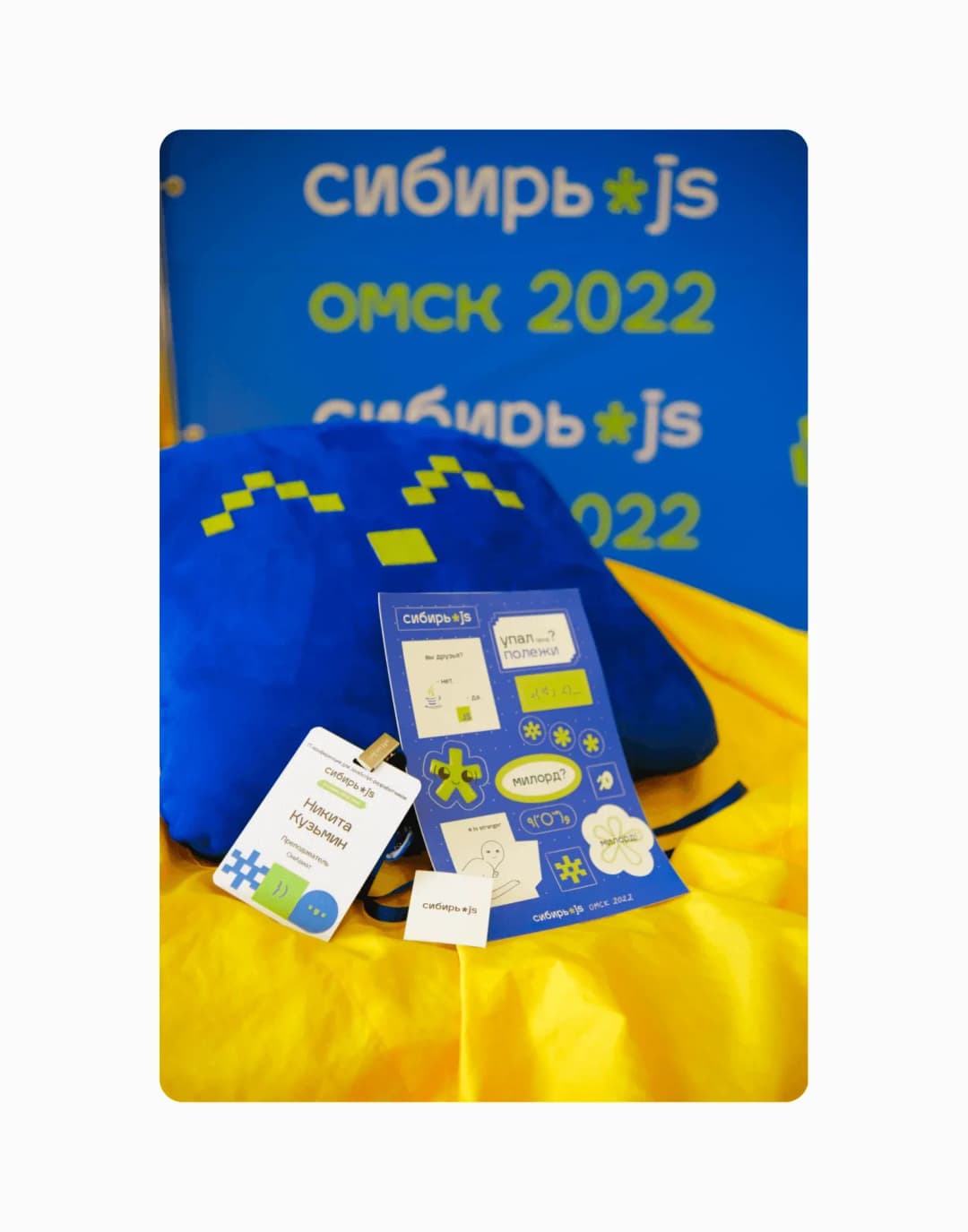 Мерч Сибирь.js: синяя подушка, бейдж и лист наклеек на жёлтом фоне