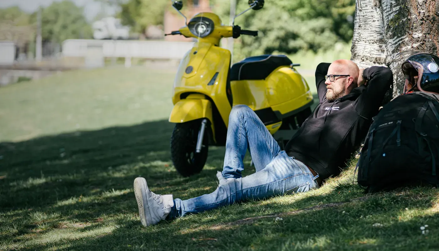 Man relaxing on grass beside yellow scooter