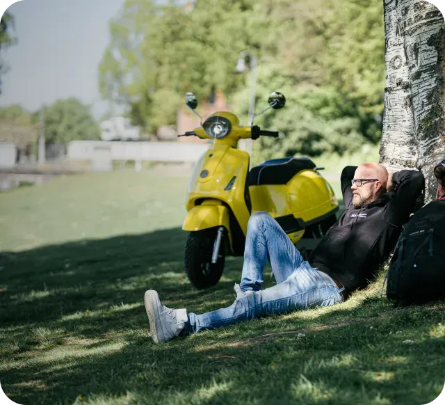 Man relaxing under a tree with a yellow scooter nearby