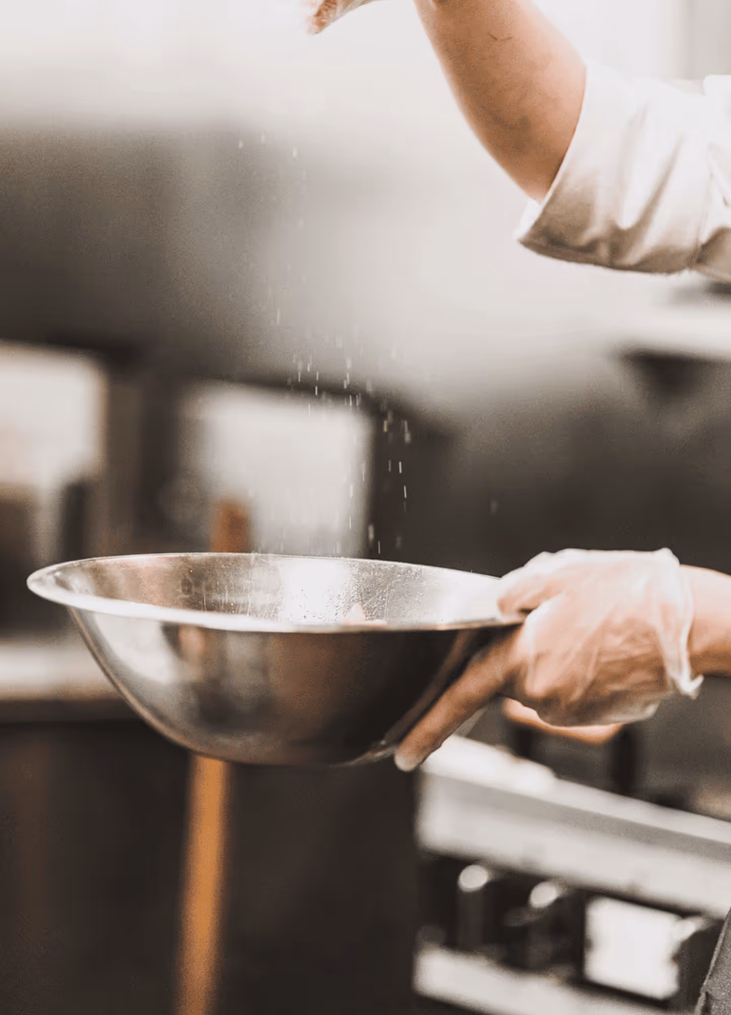 Hands sprinkling salt into a mixing bowl